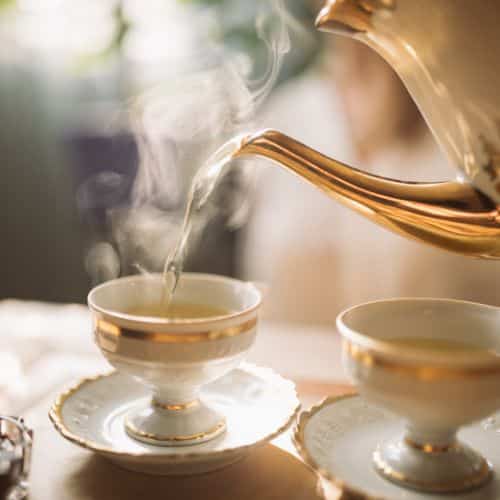 A steaming cup of tea is poured from a pot.