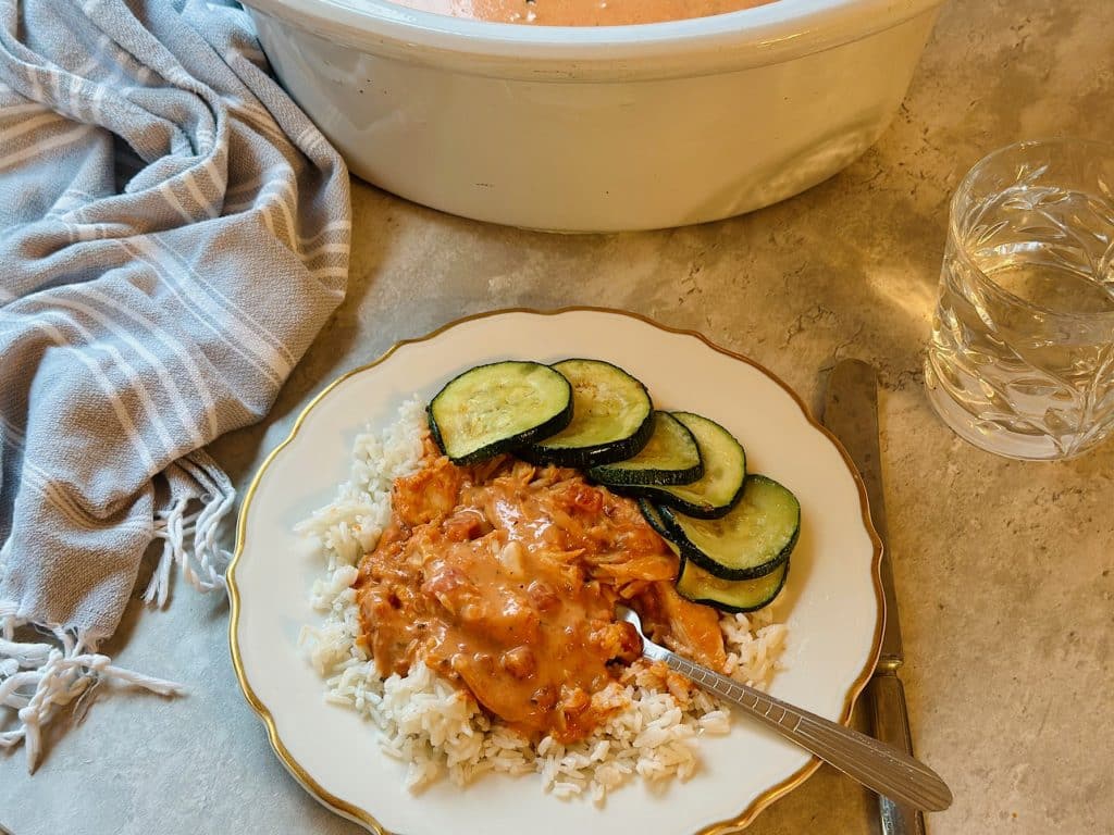 A plate of rice smothered in slow-cooker Butter Chicken Sauce with Crockpot in background.